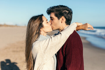 Beautiful couple in love kissing each other while enjoying the day in a cold winter on the beach.