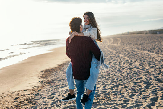 Beautiful young couple in love playing and enjoying the day in a cold winter on the beach.