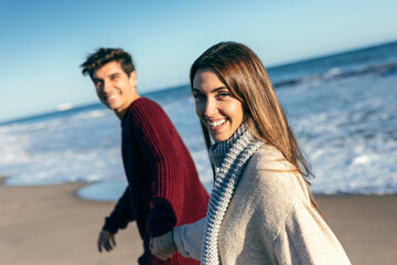 Beautiful couple holding hands while walking in a cold winter on the beach.
