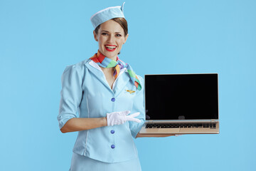 smiling female stewardess on blue showing laptop blank screen