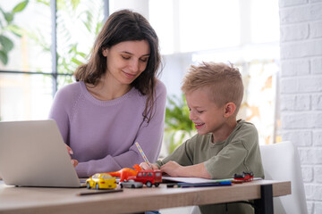 Work from home and family education, Mom and son using remote access technology for learning and work, woman works on laptop, child writes in textbook