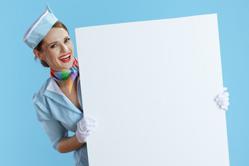 smiling modern female stewardess on blue showing blank board