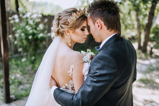 A stylish young groom in a suit and a beautiful model bride with a diadem, a crown on her head are gently hugging outdoors. Close-up wedding photography, portrait of happy newlyweds.