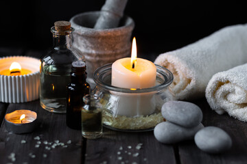Obraz na płótnie Canvas Spa setting with essential oil, candle, sea salt, pebbles, towel on dark wooden background. Massage, aromatherapy. Natural organic ingredients for relaxation, detention. Wellness in salon concept