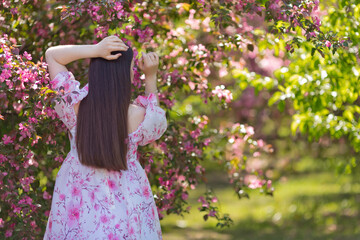 rear view, girl in a pink dress standing near pink blooming garden