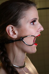 Devotes BDSM Fetisch Model mit roten Lippen, roten Kontaktlinsen, Halsreif und Mundspreizer / Knebel
