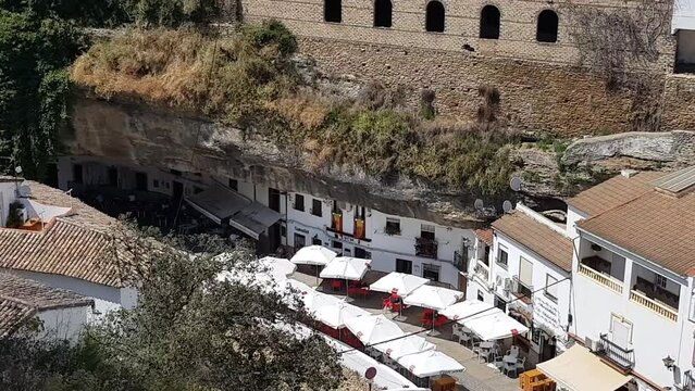 People have dinner under a huge hanging rock in Setenil de las Bodegas, Spain
