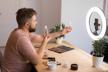 Portrait of happy man beauty blogger sitting in room at table and speaking recommending foundation or decorative cosmetic looking at camera. Blogging and vlog concept