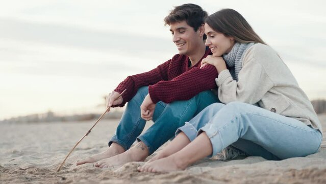 Video of beautiful couple in love drawing a heart in the sand with a stick enjoying the day on the beach.