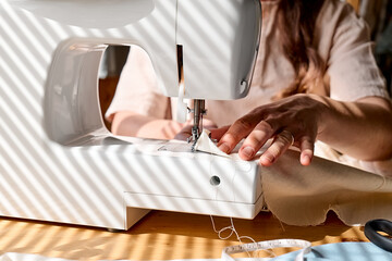 Seamstress sewing linen fabric on sewing machine in small studio. Fashion atelier, tailoring, handmade clothes concept. Slow Fashion. Conscious consumption.