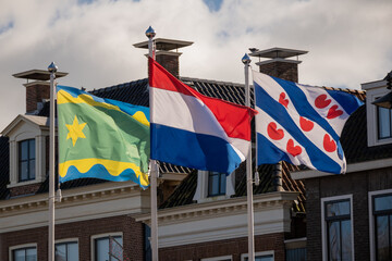 national flags of netherlands, or Nederland in Dutch, not Holland, Friesland and Noardeast Fryslân northeast proudly flying outside in Dokkum street de Dijk near residential houses on sunny day