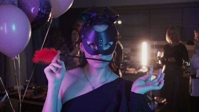 Masquerade party - a woman in a black masquerade mask plays with a camera with a feather tickler