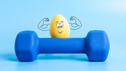 Funny Easter egg with cute face shows his muscles behind dumbbell on blue background. Strong...