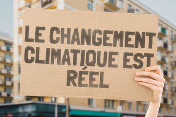 The phrase " Climate change is real " drawn on a carton banner in men's hands. Sustainability. Emissions. Renewable. Conservation. Adaptation. Carbon. Ocean. Atmosphere. Recycling. Drought. Melting