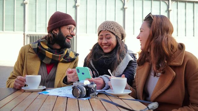 Group of young friends having fun watching videos on a social media app using a cellphone device it a coffee shop terrace. Three happy people smiling taking a selfie with a smart phone. Slow motion