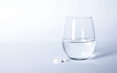 two pills with a glass of water on a white background, concept of medicine, medication, vitamins, healthy lifestyle
