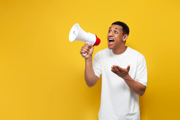 young African American guy in white T-shirt announces the news through loudspeaker on yellow...