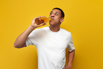 african american guy in white t-shirt drinks beer on yellow isolated background, man likes alcohol