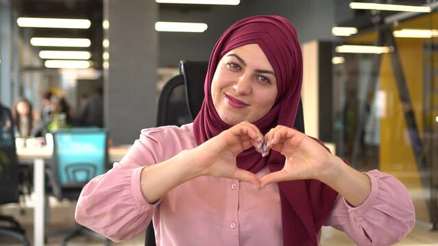 Portrait muslim woman show heart sign make symbol with hands feels grateful smile looks at camera standing indoors. Love support demonstration, volunteering, donation, good deed