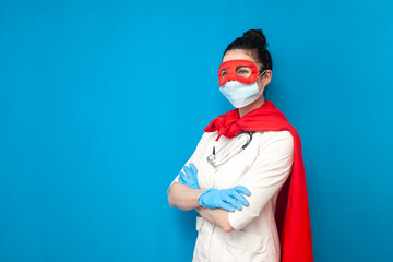 cheerful young girl doctor in uniform in superman costume on blue background, female nurse in...