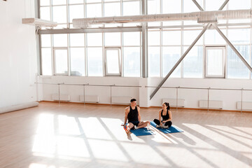 couple in sportswear sitting on yoga mats in spacious hall in the morning, athletic man and woman sitting on workout