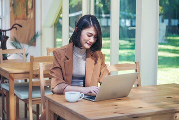 Happiness Asian Woman working from home using laptop online meeting in home office. Happy relax time asian business woman typing keyboard use notebook laptop Smiling, laughing at home office.