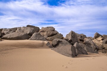 Sandy beach with boulders, large rocks. Blue sky with wispy clouds on a winter's day, Sandy Hook Beach, New Jersey, USA, part of Gateway National Recreation Area, known for hiking, camping, birding.