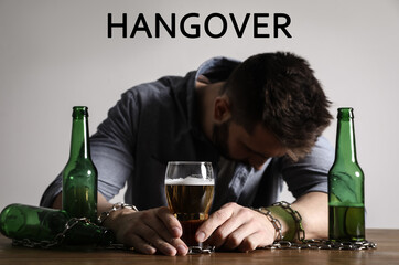 Suffering from hangover. Man chained to glass of beer at table