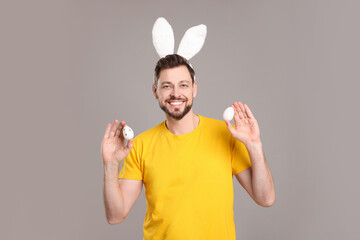 Happy man in bunny ears headband holding painted Easter eggs on grey background