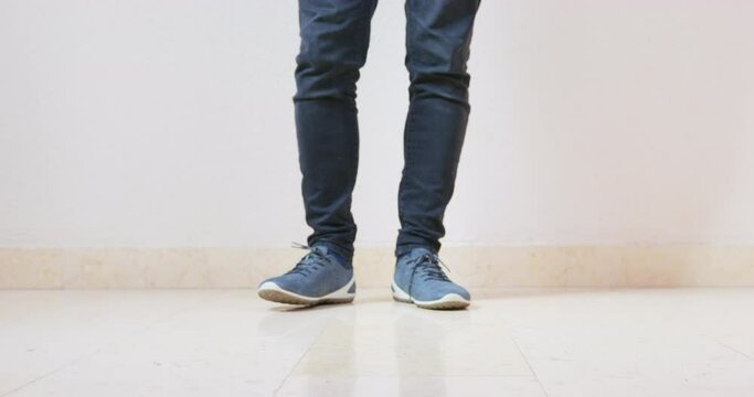 Dressed dachshund dog runs past man in snickers tapping foot. Black domestic animal in blue t-shirt and male owner against white wall closeup