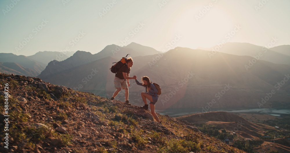 Wall mural caucasian girl climbing up a mountain, getting hand of help from her partner, adventuring and explor