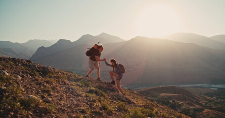 Caucasian girl climbing up a mountain, getting hand of help from her partner, adventuring and...