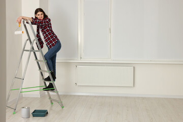 Young beautiful woman with roller on metal stepladder indoors. Room renovation