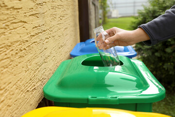 Fototapeta na wymiar Woman throwing glass bottle into recycling bin outdoors, closeup