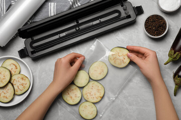 Woman packing cut eggplant into plastic bag using vacuum sealer on light grey marble table, closeup