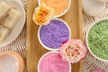 Bowls with sea salt, soap bars, jar of cream and roses on wicker mat, flat lay