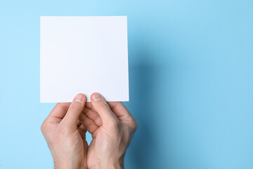Fototapeta premium Man holding sheet of paper on light blue background, top view. Mockup for design