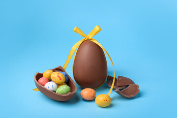 Tasty whole chocolate eggs with yellow bow and different candies on light blue background