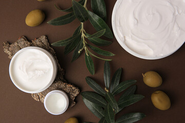 Flat lay composition with jars of cream and olives on brown background