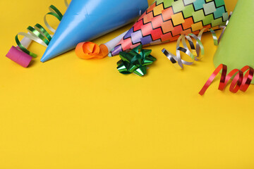 Party blowers, hats and streamers for birthday party on yellow background. Space for text