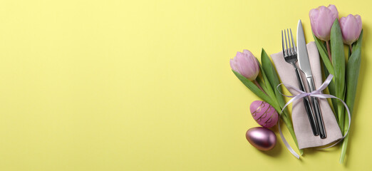 Set of cutlery, Easter eggs and tulips on yellow table, top view. Banner design with space for text