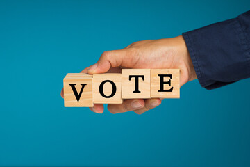 Close-up of hand holding wooden cubes with letters VOTE against a blue background