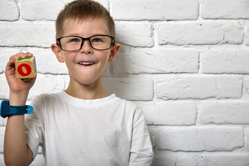 Happy boy stands against white brick wall with cube in hand, colored letters alphabet on cube....