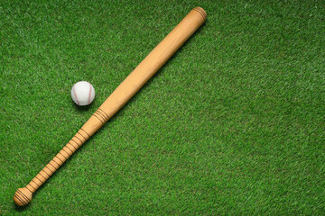 Fototapeta na wymiar Wooden baseball bat and ball on green grass, flat lay. Space for text
