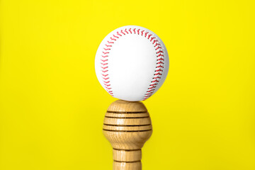 White ball on wooden baseball bat against yellow background, closeup. Sports equipment