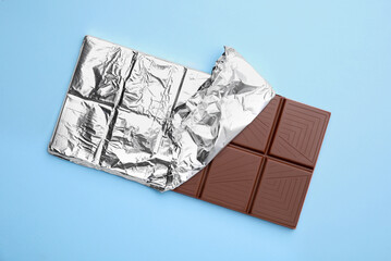 Tasty chocolate bar on light blue background, top view