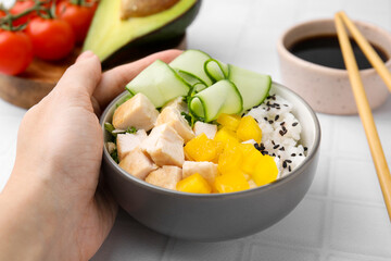 Woman holding delicious poke bowl with meat, rice and vegetables at white table, closeup