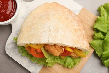 Delicious pita sandwich with fried fish, pepper, tomatoes and lettuce on light grey table, flat lay
