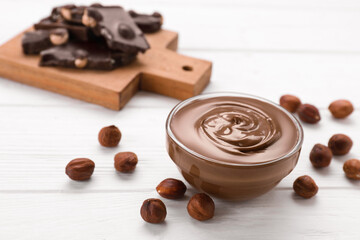 Bowl with tasty paste, chocolate pieces and nuts on white wooden table. Space for text