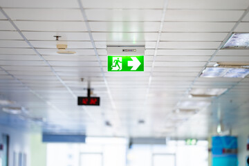 Green White light neon sign depicting a fire exit with interior mirror door background. It's hung...